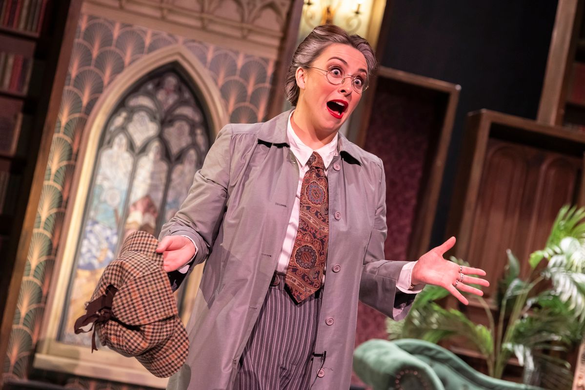 Performer in period costume and round glasses gestures while holding a deerstalker hat