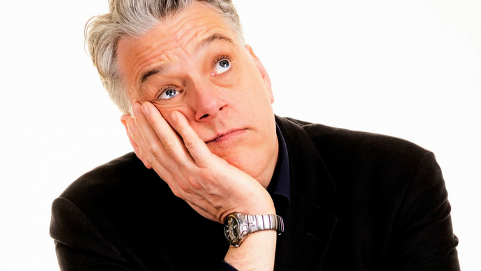 Performer rests head on hand and looks upward against a plain white background