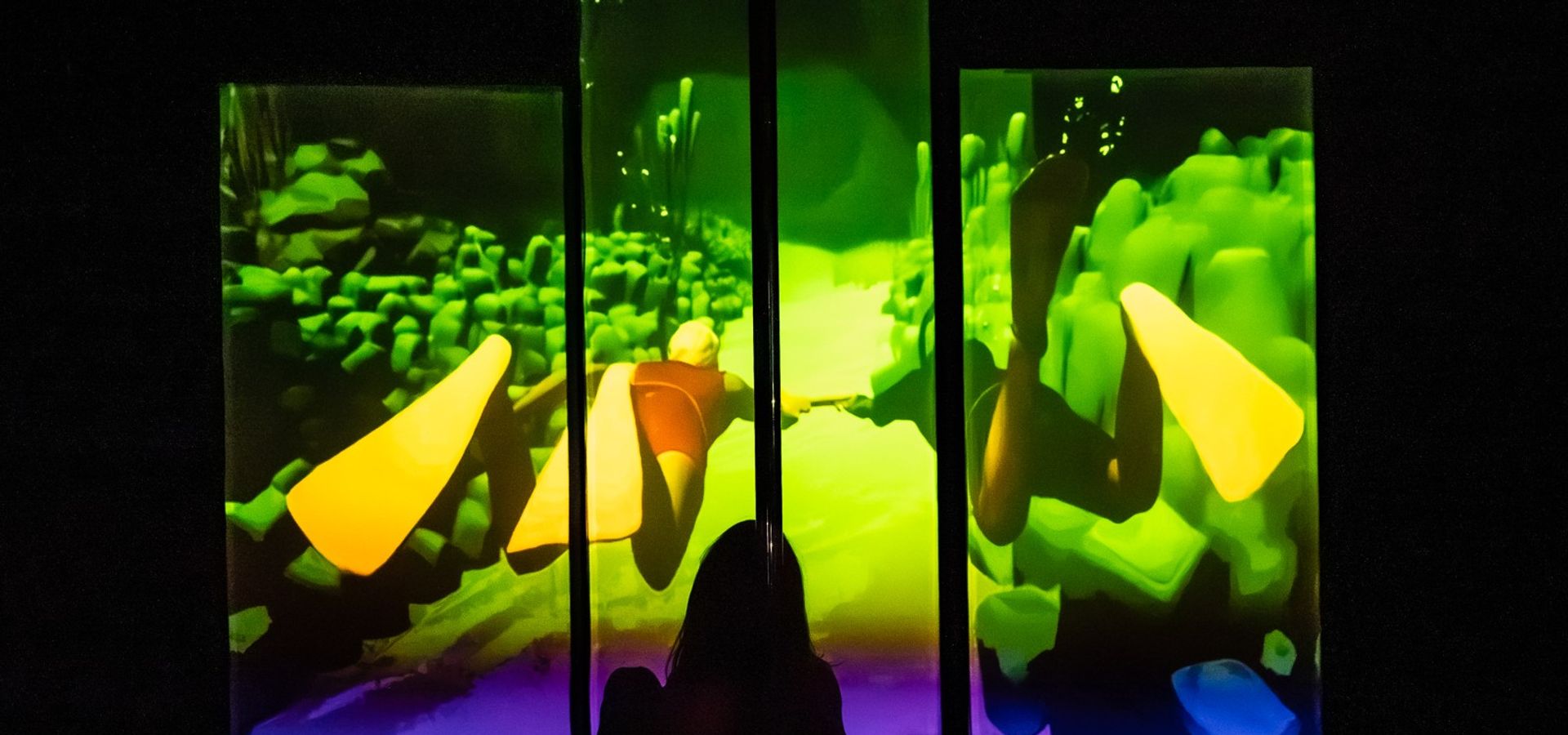 Silhouetted figure sits before illuminated panels showing an underwater scene with a diver and bright yellow fins.